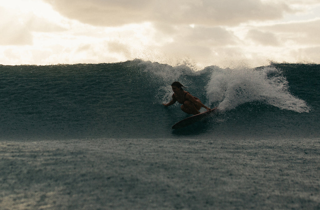 Woman doing a crouched bottom turn on surfboard in the rain