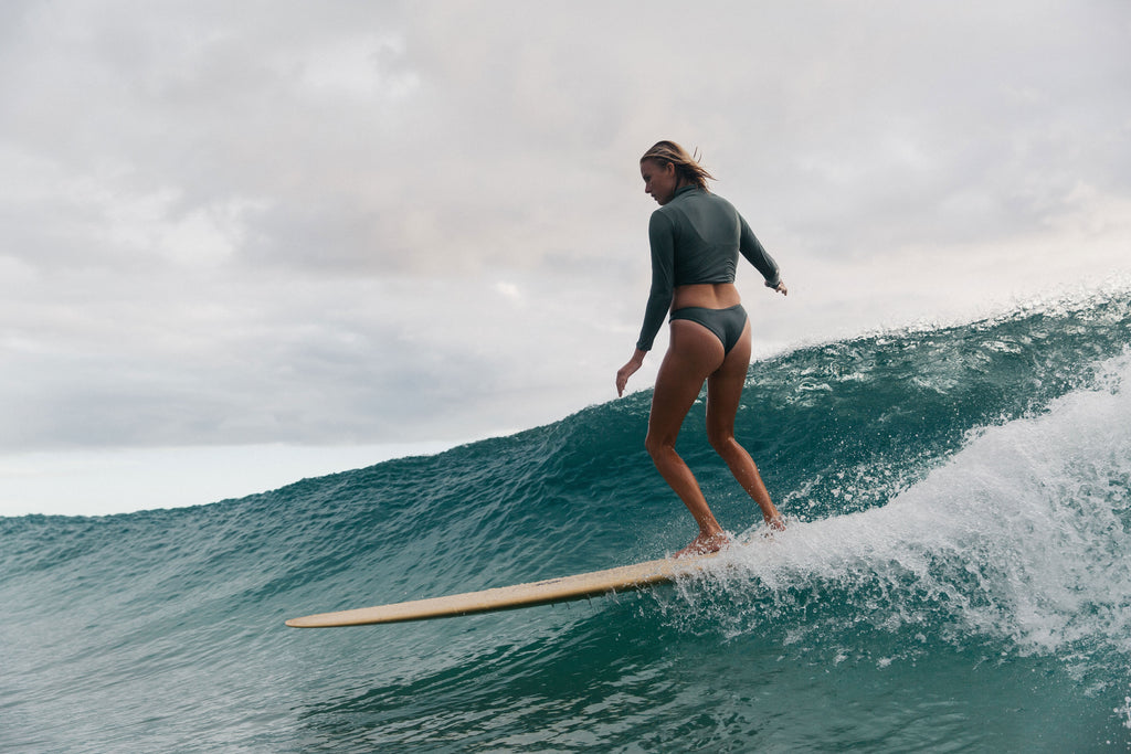 Woman surfing down the line in a rash guard and surf bikini bottom in army green