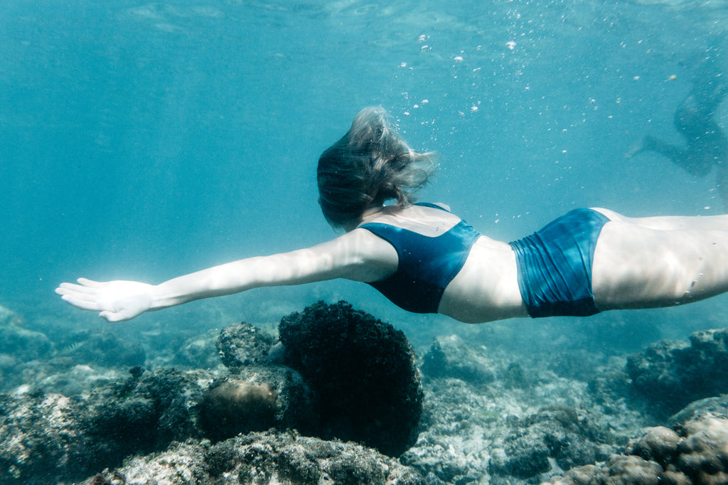 underwater photo of woman swimming past coral reef wearing a surf bikini in bottle green