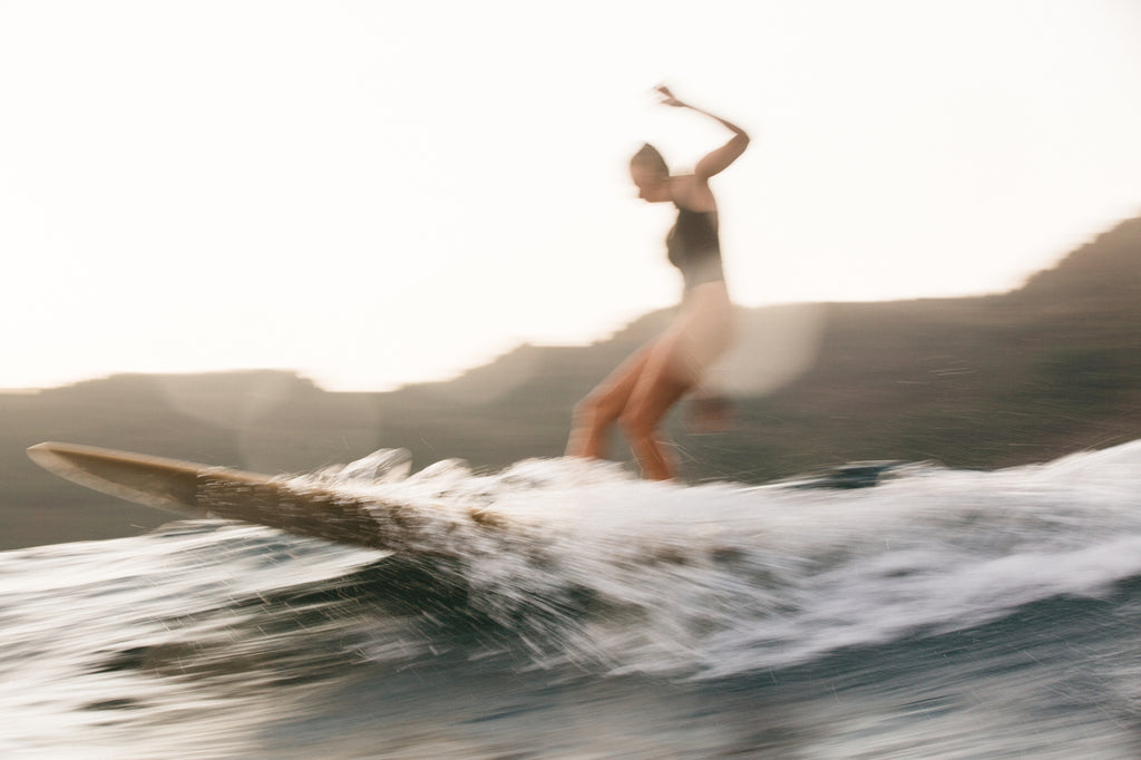 Speed blur photo of woman surfing in a black one piece surf swimsuit