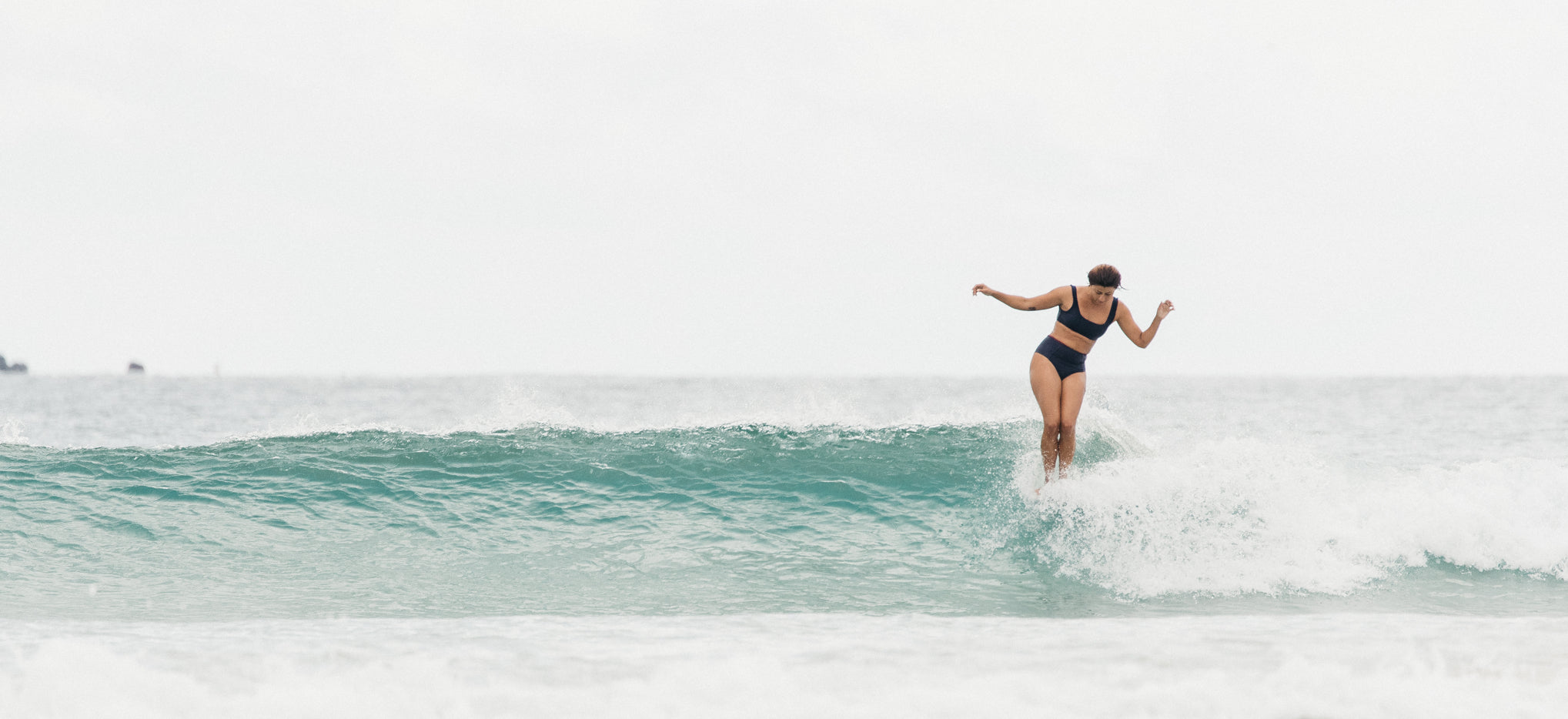 Woman surfing and riding the waves, wearing SEPTEMBER The Line sustainable surf and swimwear.