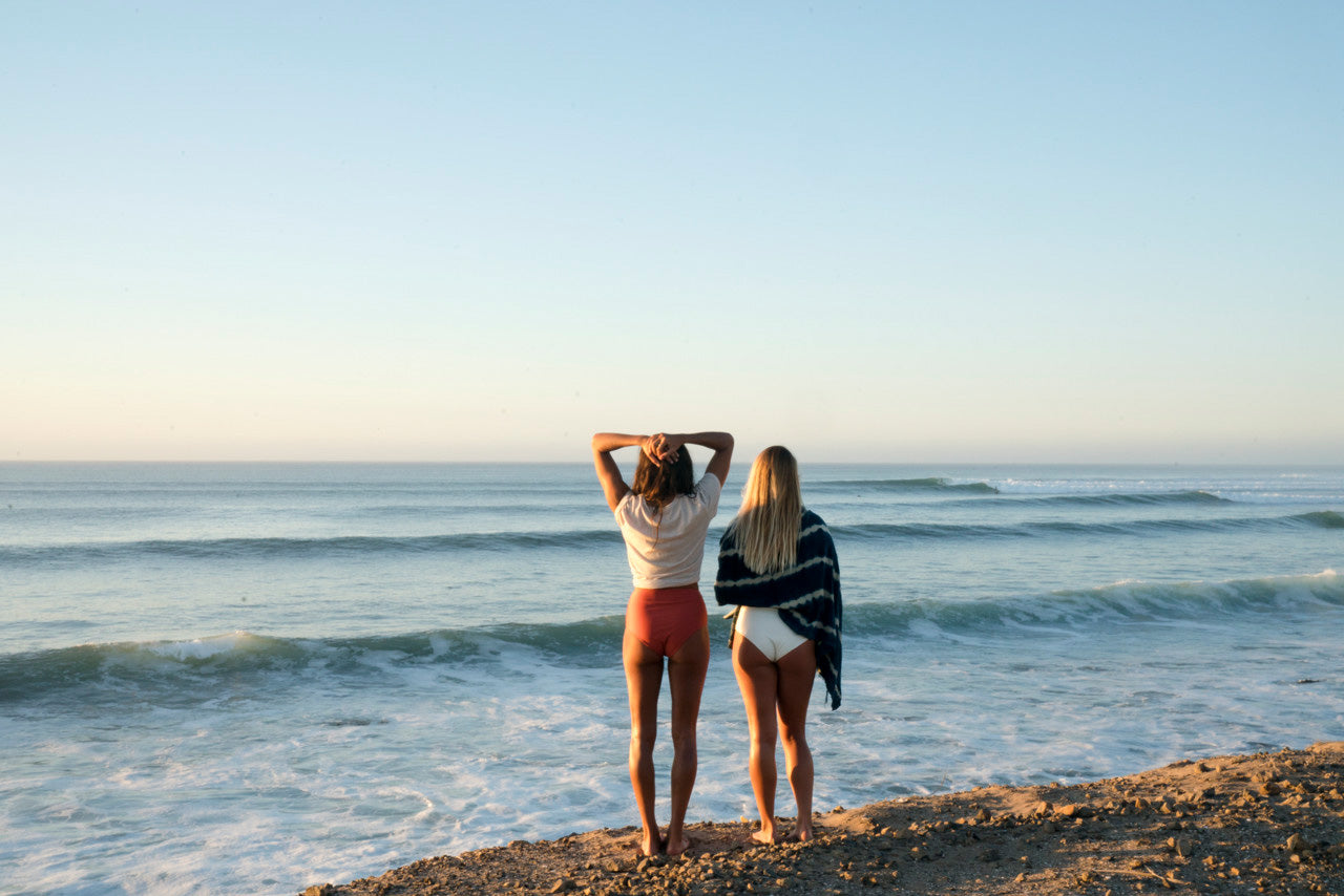 Two women standing on a cliff looking at the surf at sunrise