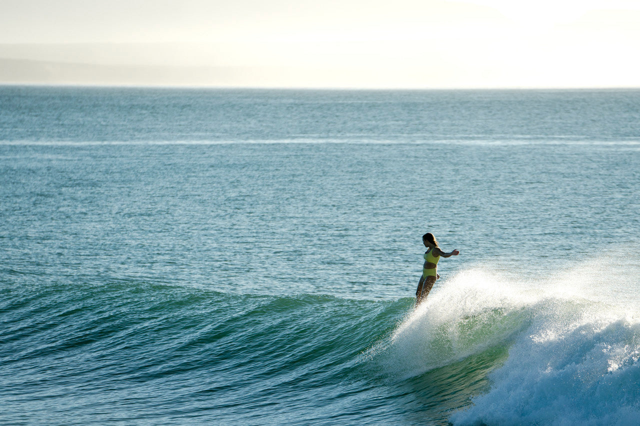 Woman surfing wearing a surf bikini top and bottom in sunflower yellow