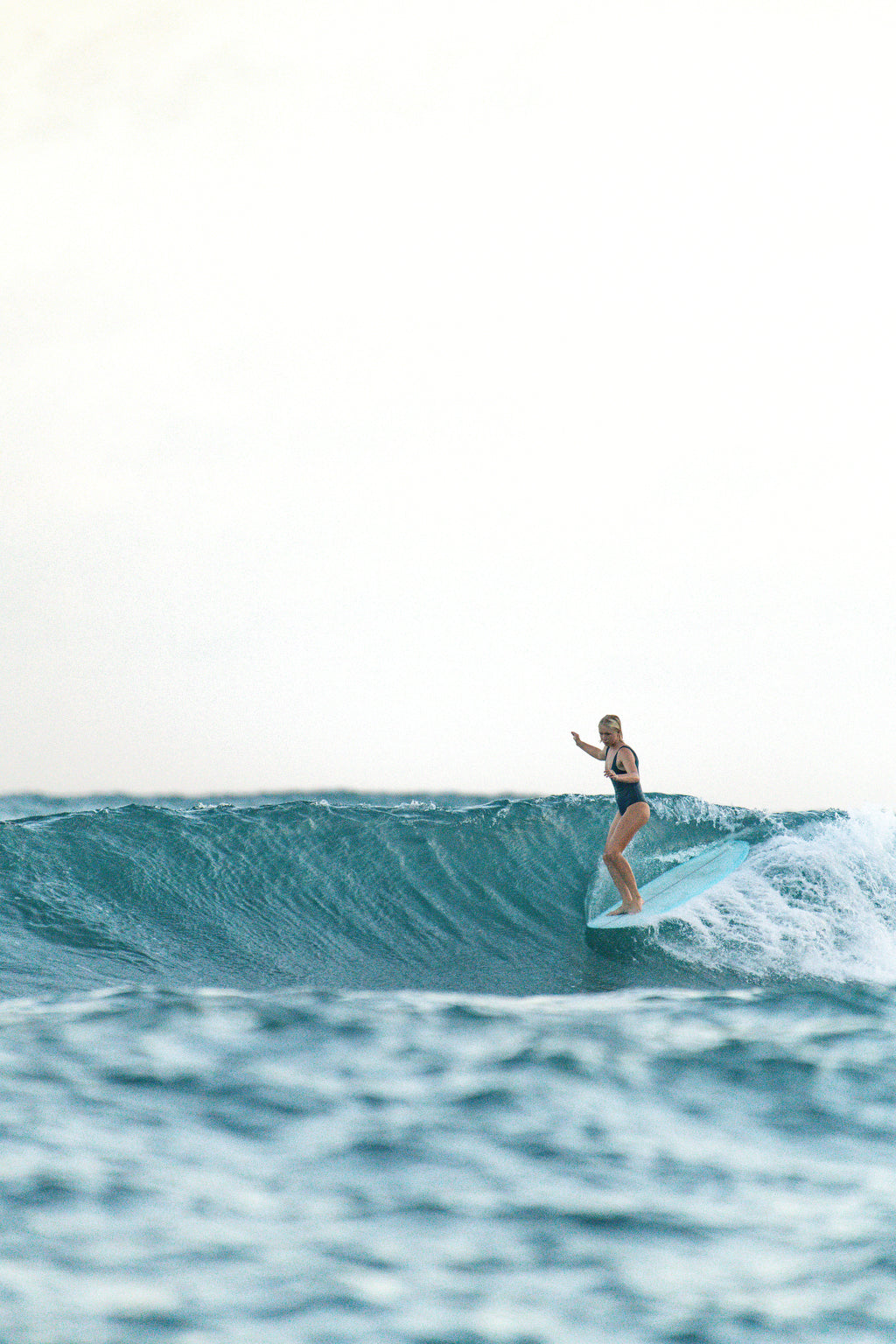 Woman surfing a longboard wearing Elena one piece surf swimsuit in Bottle Green