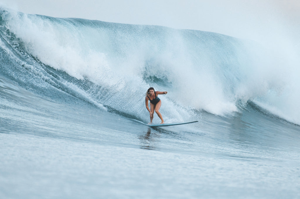Woman doing a bottom turn on overhead wave wearing Miller one piece surf swimsuit in Bottle Green
