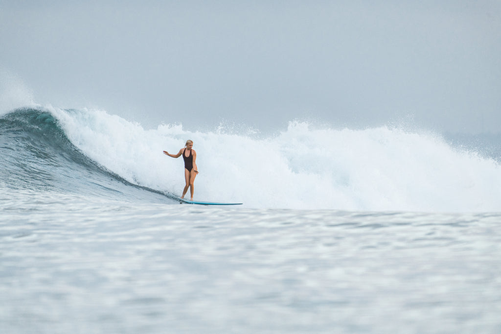 Woman doing a bottom turn on surfboard wearing the Elena piece surf swimsuit in Indigo