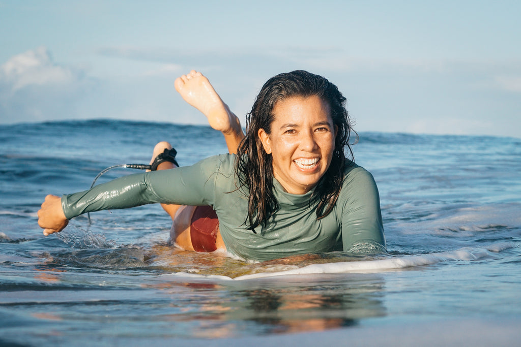 Erika smiling and paddling in the water wearing a rash guard and lucky high waisted surf bikini bottoms