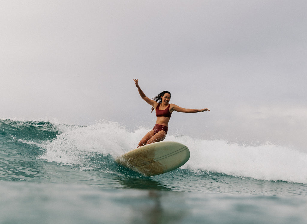 Woman wearing the mason surf bikini top and kennedy surf bikini bottom doing a carving turn on her surf board.