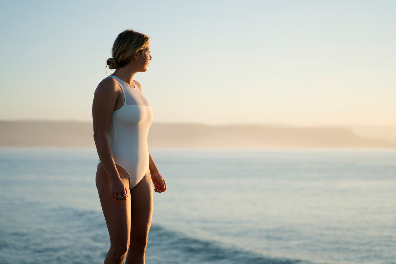 Silhouette portrait of a woman at sunrise looking at the ocean wearing Infinite one piece surf swimsuit in ivory