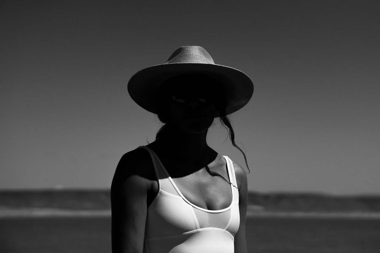 Woman wearing a straw hat and james one piece surf swimsuit standing on the beach