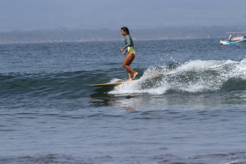 Erika cross stepping on a longboard wearing a rash guard and high waisted surf bikini bottoms