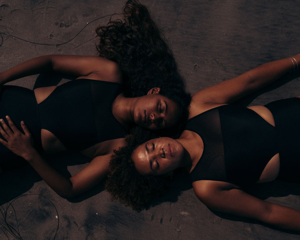 Two women laying on beach wearing black swimsuits