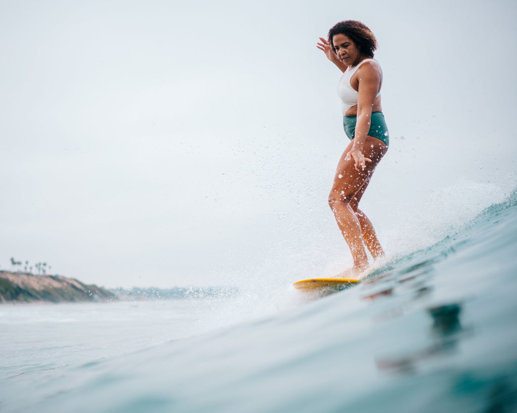 Woman going backside on a longboard surfing in ivory army one piece swimsuit