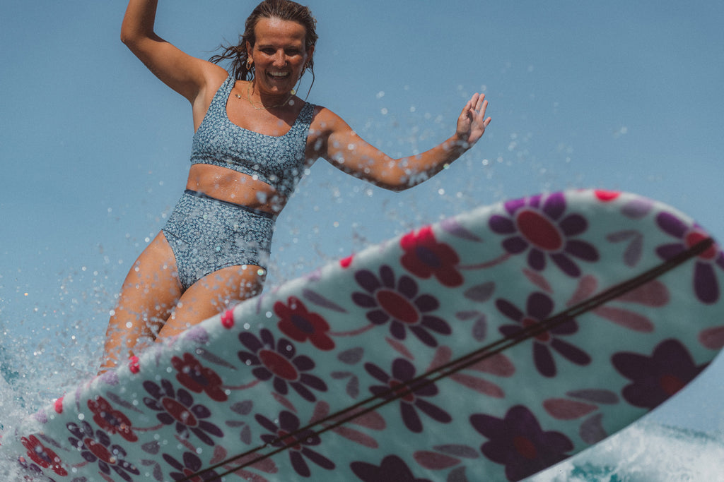 Woman surfing on a longboard smiling wearing a SEPTEMBER surf bikini