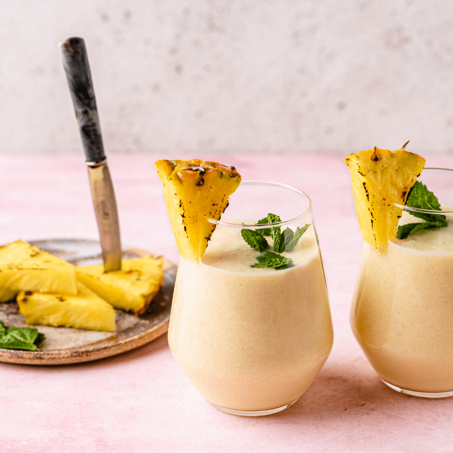 Pineapple and collagen mocktails with pineapple wedges on side of glassware. 