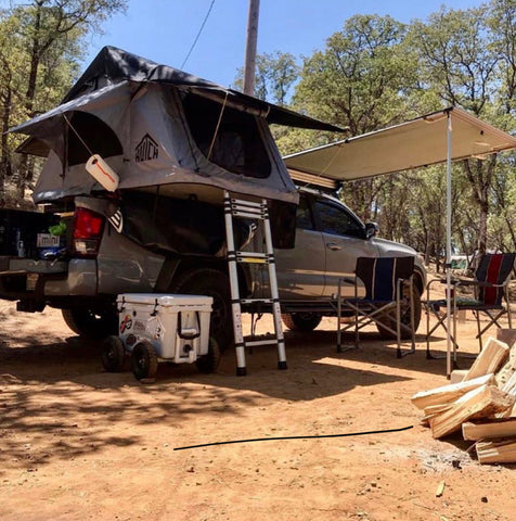 A rooftop tent is deployed on a pickup truck on a small campsite.