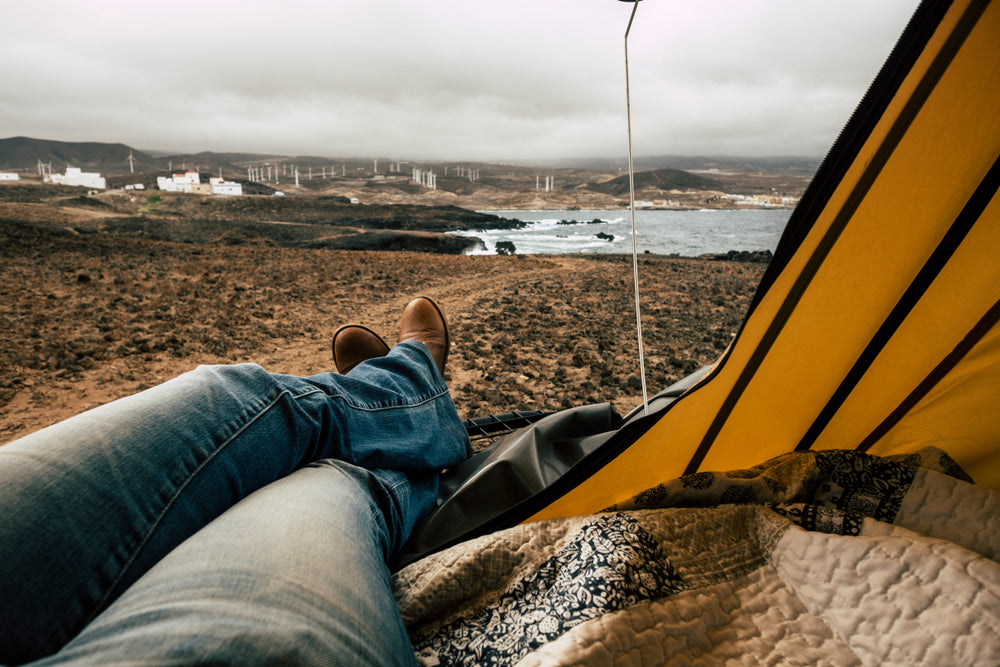 A person inside a roof top tent relaxing and looking at the view