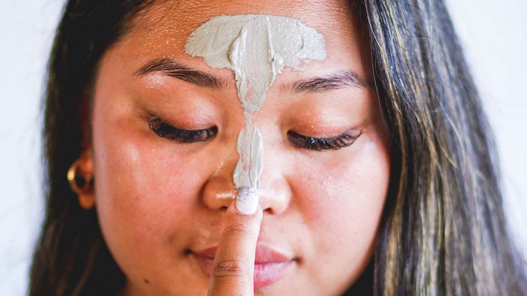 Woman applying salicylic acid face mask to acne skin