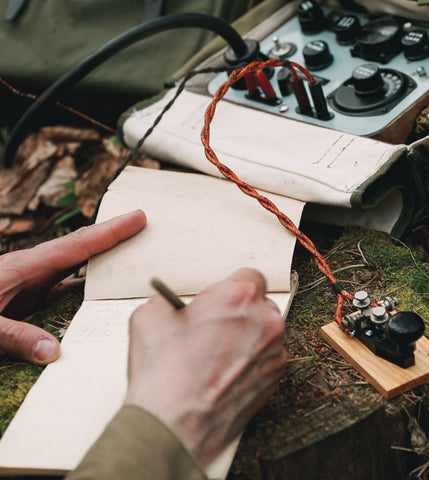 soldier's hand writing message next to a telegraph machine