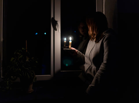 woman in a darkened house holding candles to see