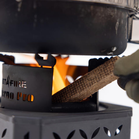 A gloved hand putting wood inside the Inferno Pro stove, keeping it ablaze.