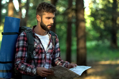 A man with bug-out supplies holding a map in the forest.