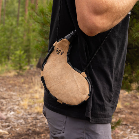 Man carrying a tan leather bota bag at his side in the outdoors.