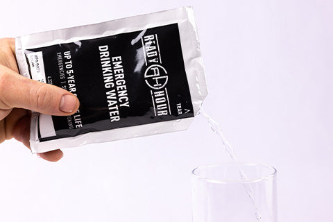 A hand pouring a pouch of Emergency Drinking Water into a glass.