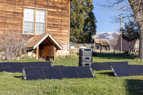 A series of solar panels set up on the front lawn of a cabin property.