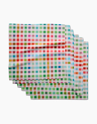 Four colorful Woven Spring Plaid Dinner Napkins by Pascale Dilger, featuring red, green, blue, orange, and yellow stripes, are stacked on a white background. Made from soft Geosuede fabric with recycled materials.