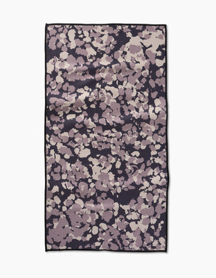 The GEOMETRY Metro Mesh is a rectangular fitness towel with an abstract lavender, mauve, and cream pattern on a dark background, bordered in black—crafted from ultra-absorbent recycled materials.