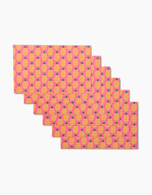 Six rectangular Daria Solak Pineapples placemats, made from eco-friendly materials, overlap in a fan arrangement and display a bright pink background with repeating yellow pineapples and green leaves.