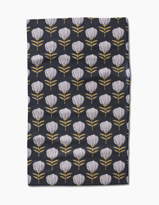 The Blomma tea towel by Anna Christian features stylized white flower heads with yellow stems in neat rows on dark fabric, made from recycled materials.