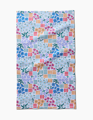 The Floral Garden tea towel by Charlie Rowan Designs features a colorful geometric and floral pattern with orange, red, green, blue, and purple flowers and leaves plus multicolored striped squares on white Geoweave fabric.