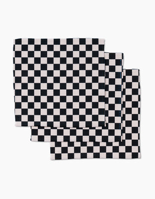 Four ultra-absorbent GEOMETRY Checkered cloth napkins, featuring a black and white checkerboard design, are neatly stacked with slight overlap on a white background.