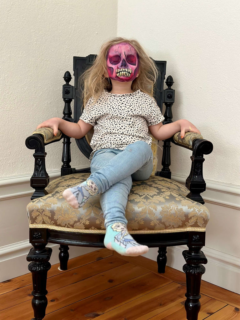 Flicka som sitter på stol med ansiktsmålning skelett