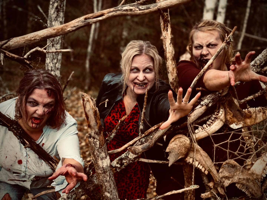 Tre stycken blodiga Zombie-tjejer i skogen bakom ett staket med skelett.