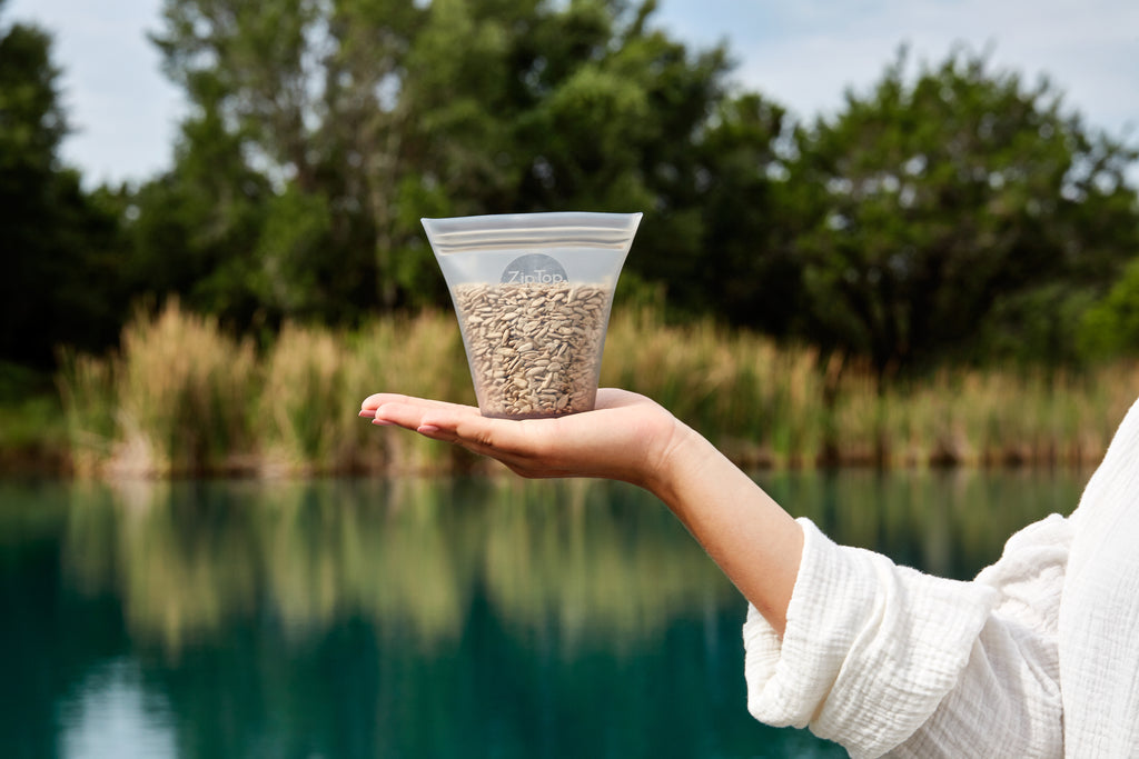 Hand holding reusable silicone container filled with sunflower seeds