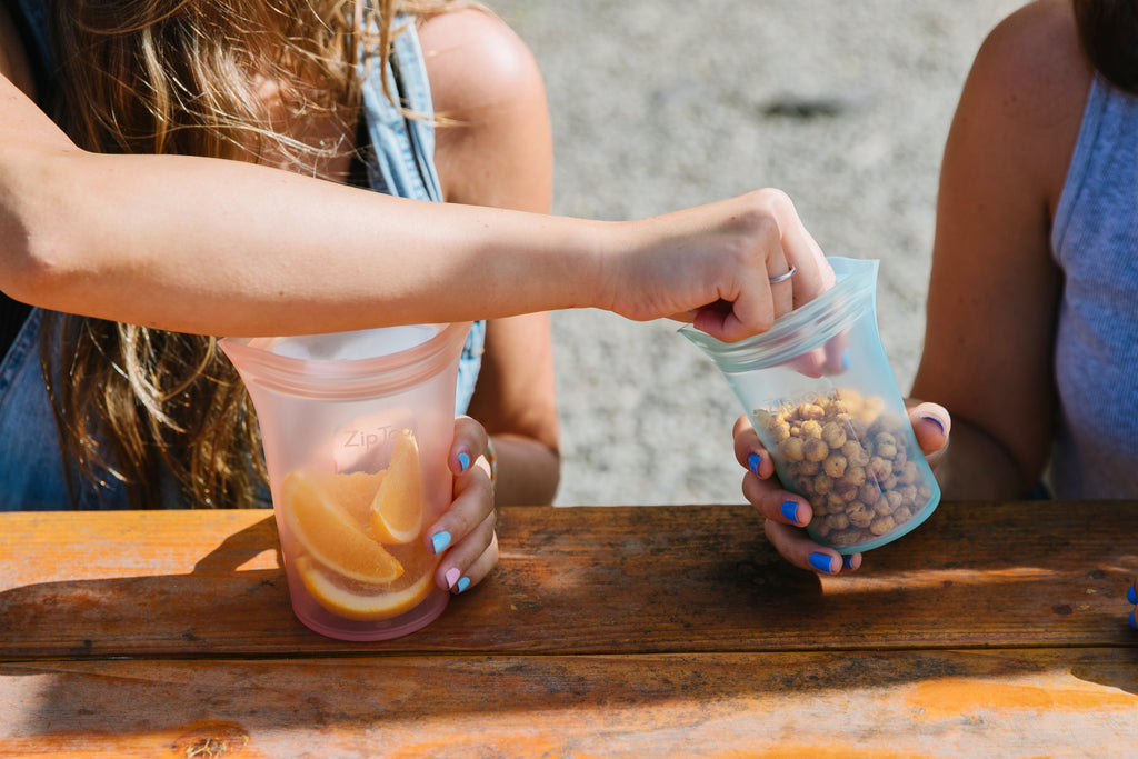 Reusable silicone bags with oranges and with pretzel balls + models sharing at picnic bench 