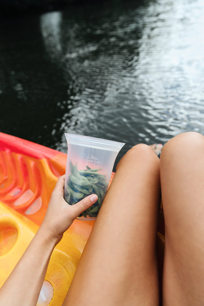 Reusable silicone bag with edamame + model holding next to legs in kayak