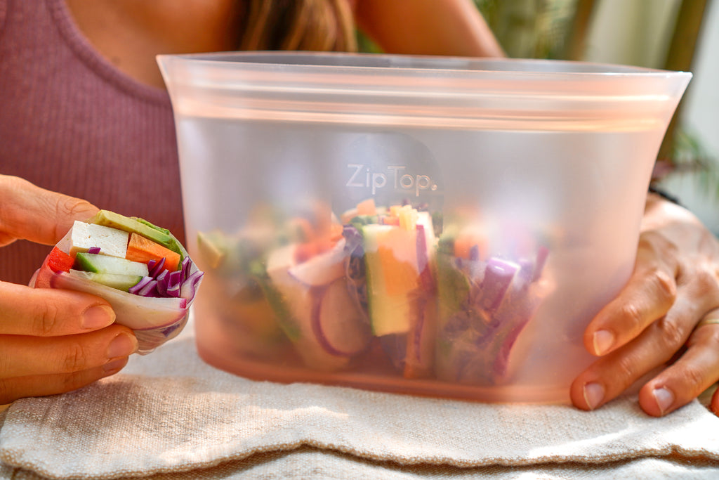 Reusable silicone container with prepared vegan spring rolls cut inside dish on outdoor table