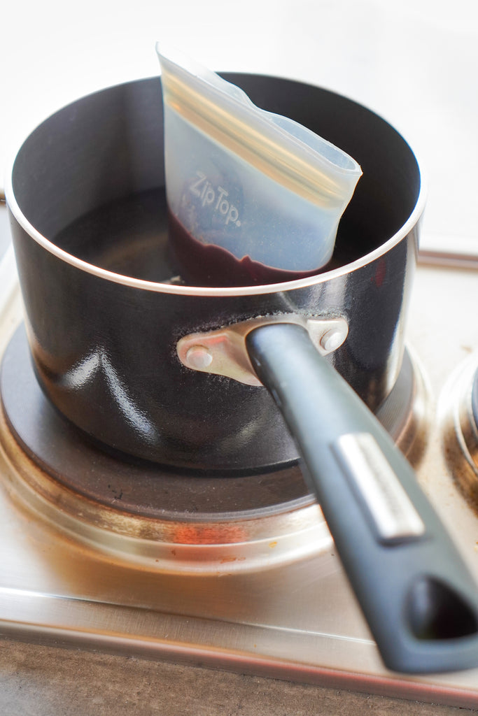 Small reusable silicone cup with chocolate melting in pot on stove