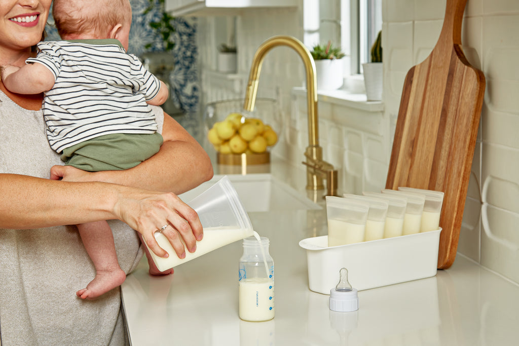 Reusable breastmilk bag set on counter with baby sitting up and mom pouring milk from bag into bottle