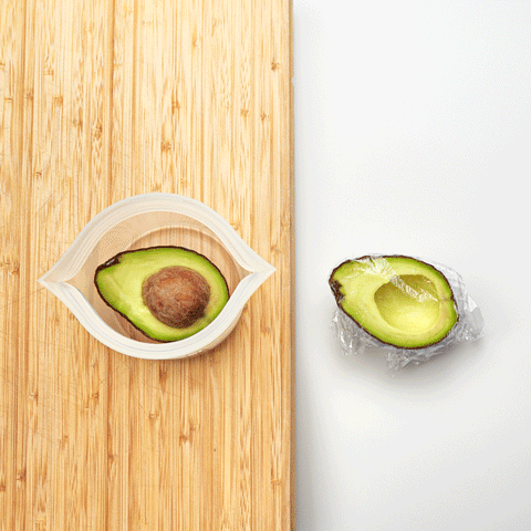 two avocado halves being stored in two different ways: one with plastic wrap and the other with a frost Zip Top cup.