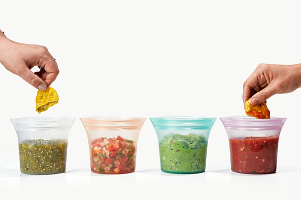 an arrangement of salsas and guac in Zip Top short cups, showing two hands dipping in tortilla chips