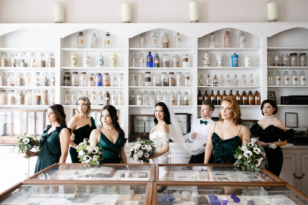 vintage drug store with bridal party in emerald green gowns as bride tries on her bridal accessories