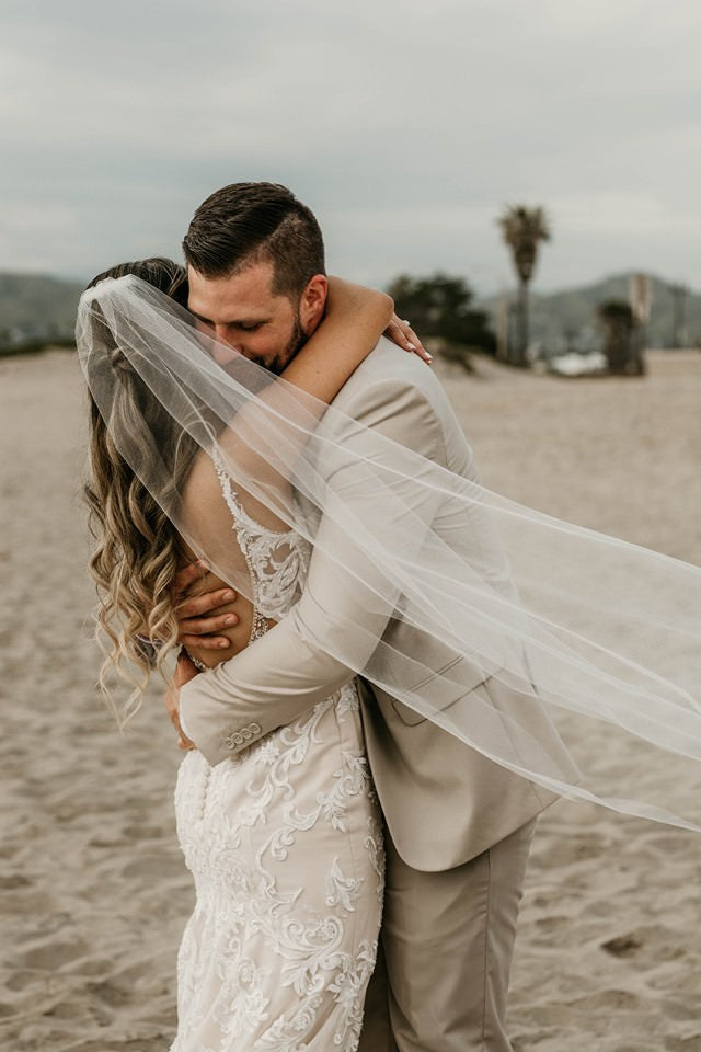 blush champagne wedding veil with nude bridal gown as bride embracing groom on beach