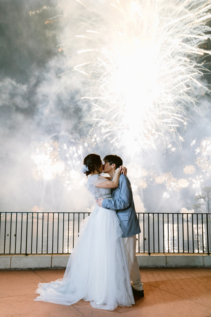 couple under Disney fireworks with bride in belle updo with tulle bow with pearls