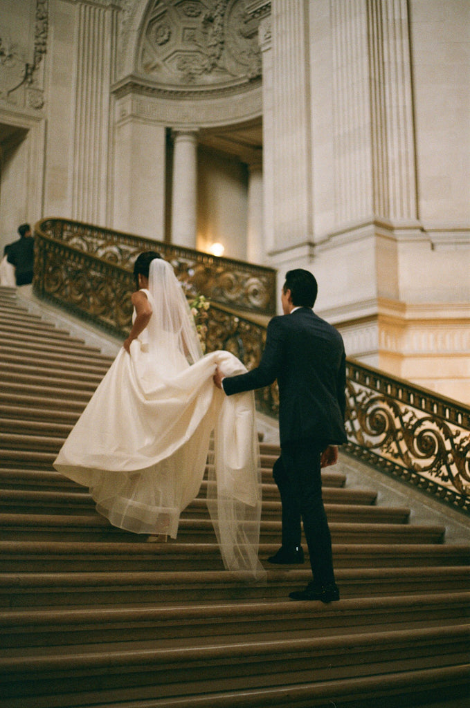 long bridal veil in  ivory for San Francisco city hall wedding with groom holding veil as they go up stairs