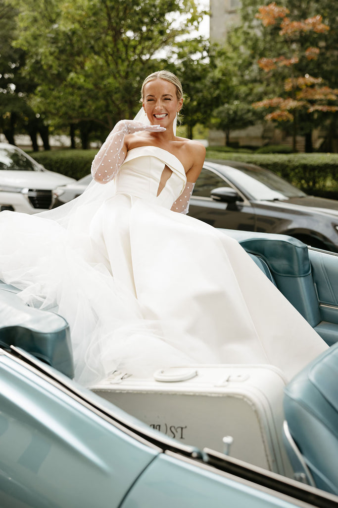 classy bride with polka dots and elegant updo sitting on vintage blue getaway car